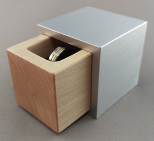 Silver aluminum cube ring box, with blonde maple wooden insert, slightly open to show silver wedding ring