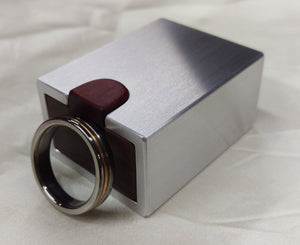 Silver metal engagement ring box with dark wood inside, men's wedding ring propped up to show scale