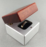 Engagement ring box with silver base and red wood lid, slightly open exposing wedding ring on black velvet