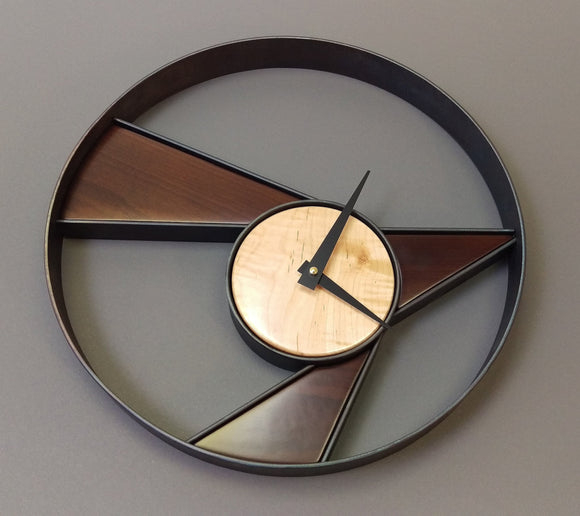 Abstract round steel wall clock, with triangular pieces of dark and light maple inlaid, black clock hands