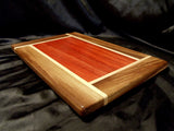 rectangular wooden cutting board. center is red padauk, framed with pinwheel rays of white maple and brown walnut