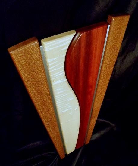 Tapered Wooden wall sculpture, brown lacewood on the outside, surrounding a centerpiece of white figured maple and red Paduak, brushed aluminum inlays