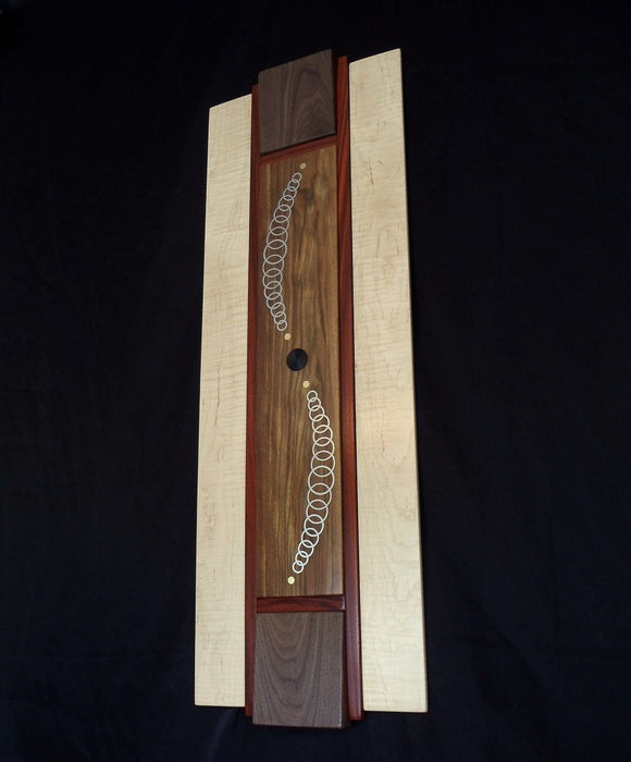 tall rectangular Wood and metal wall art. white maple with brownish yellow canary wood. An s curve of progressively sized metal rings inlaid into center tile